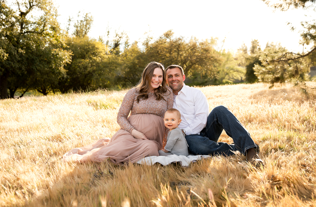 Man and pregnant woman sitting in a field with a toddler.