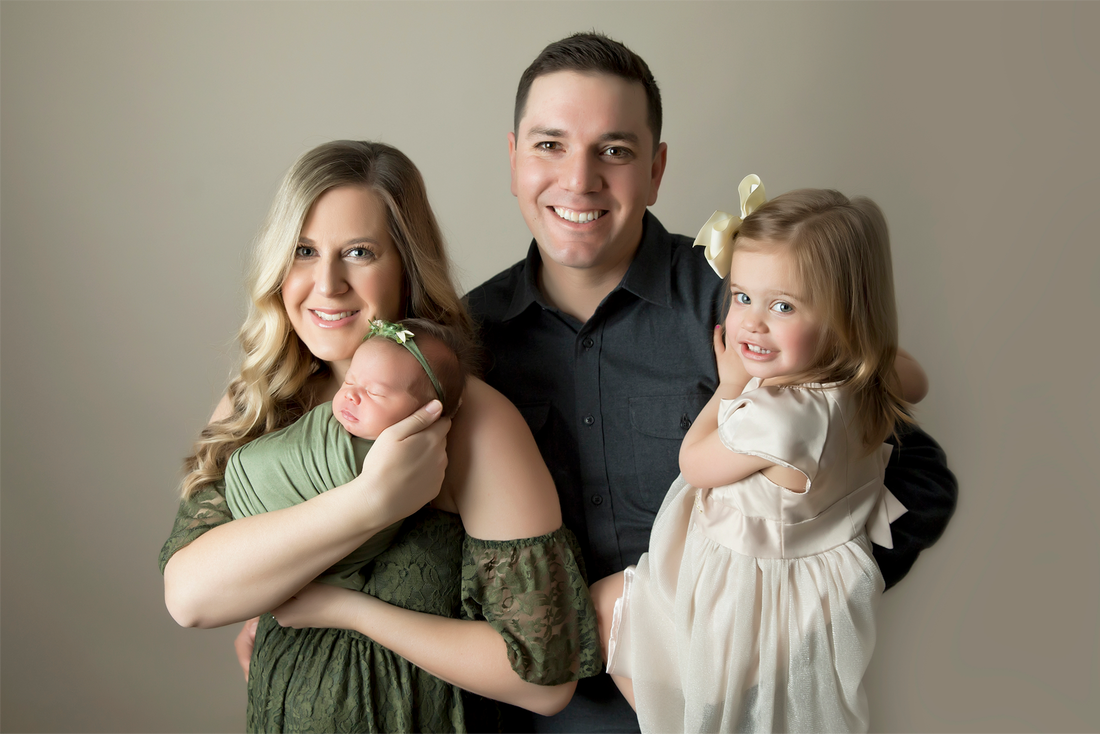 Man and woman with newborn baby and little girl in front of neutral background.