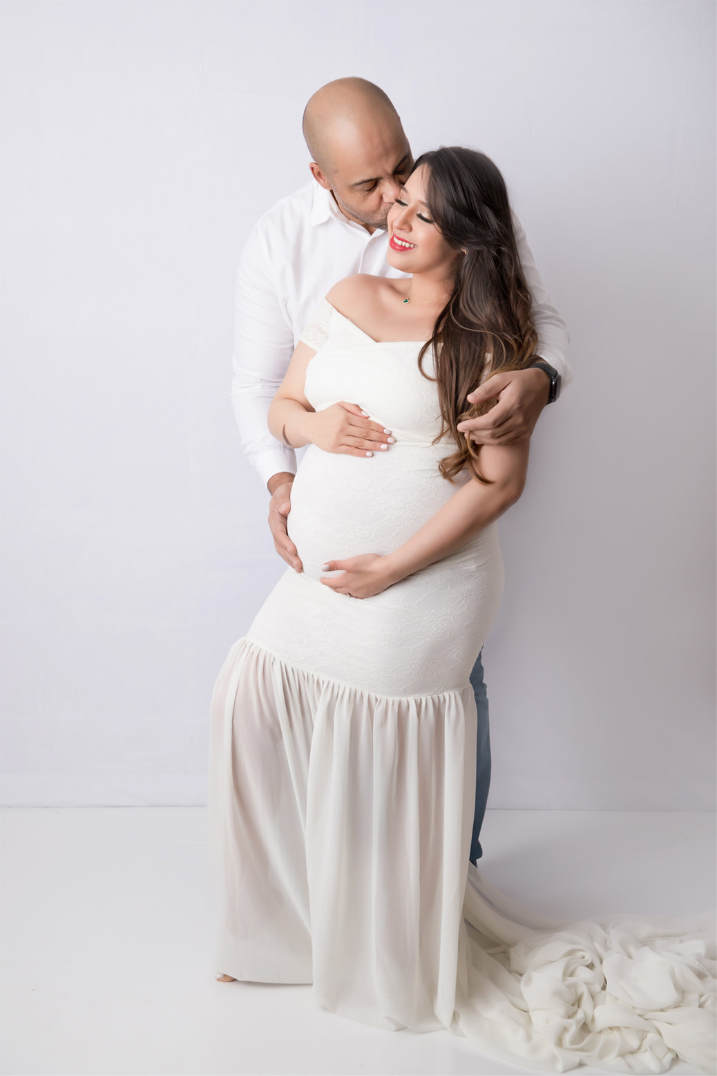 Man holding pregnant woman's belly, both wearing white in front of white backdrop
