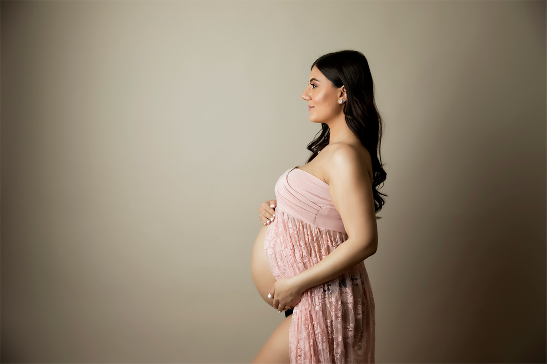 Woman holding pregnant belly in pink dress. Tan background