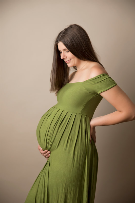 Woman holding pregnant belly in green dress. Tan background