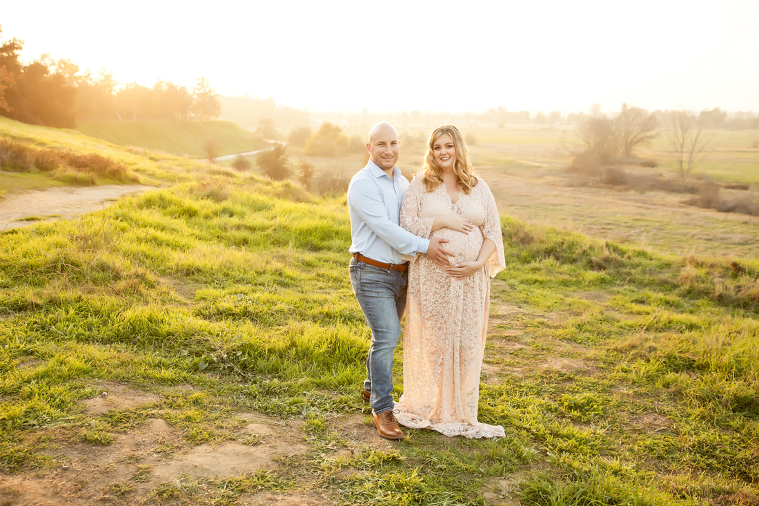 Man holding woman's pregnant belly, she is wearing a dress and he is wearing a blue shirt and jeans