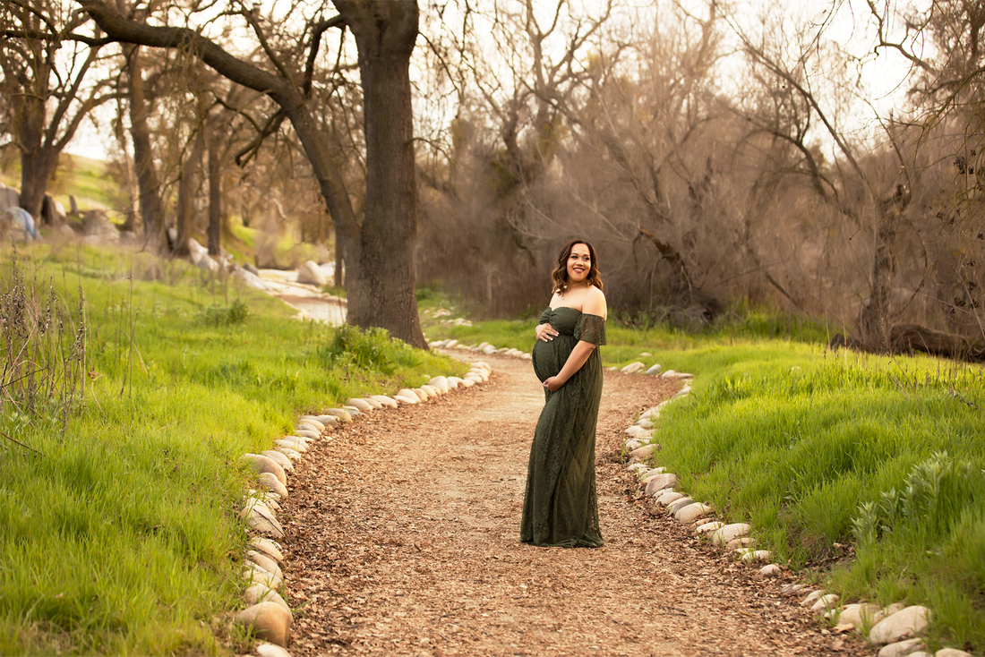 Pregnant woman standing in green dress on a path in wooded area