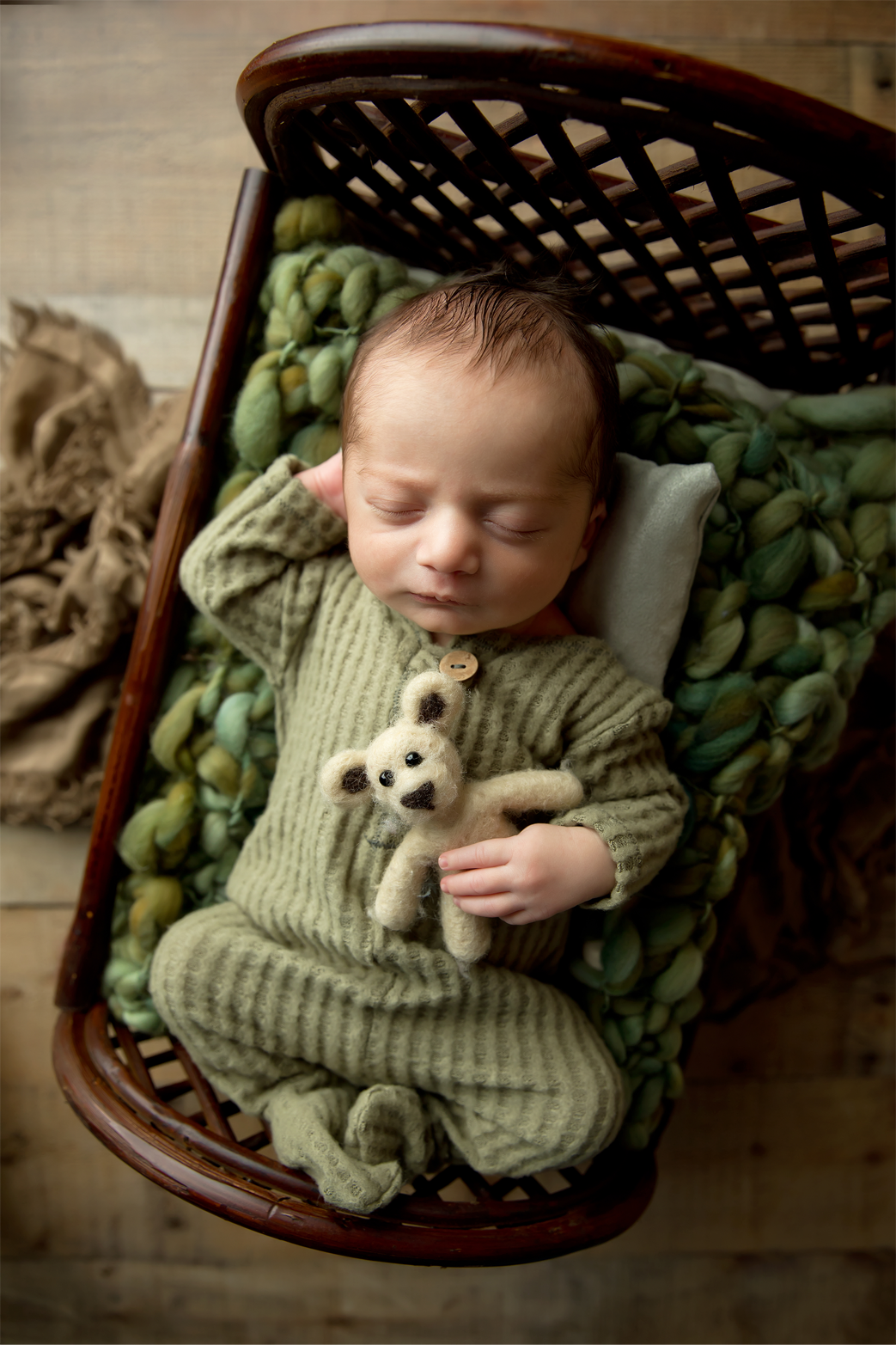 Sleeping baby boy in a green outfit on a bed with green props and tiny teddy bear.