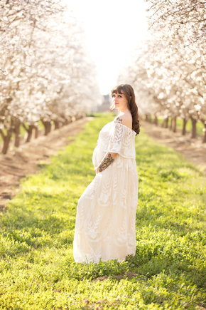 Woman holding her pregnant belly in a field of blossoms, wearing a white lace dress