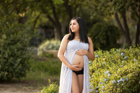 Woman looking into the distance wearing an exposed belly shirt, she is holding her pregnant belly