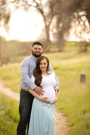 Man standing behind pregnant woman holding her belly, standing in green field