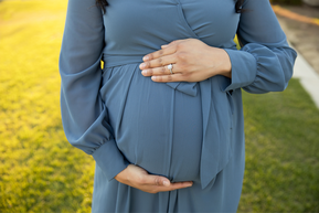 Woman in blue dress holding her pregnant belly, grass behind her