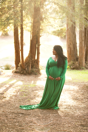 Pregnant woman standing in front of trees, she is wearing a bright green dress