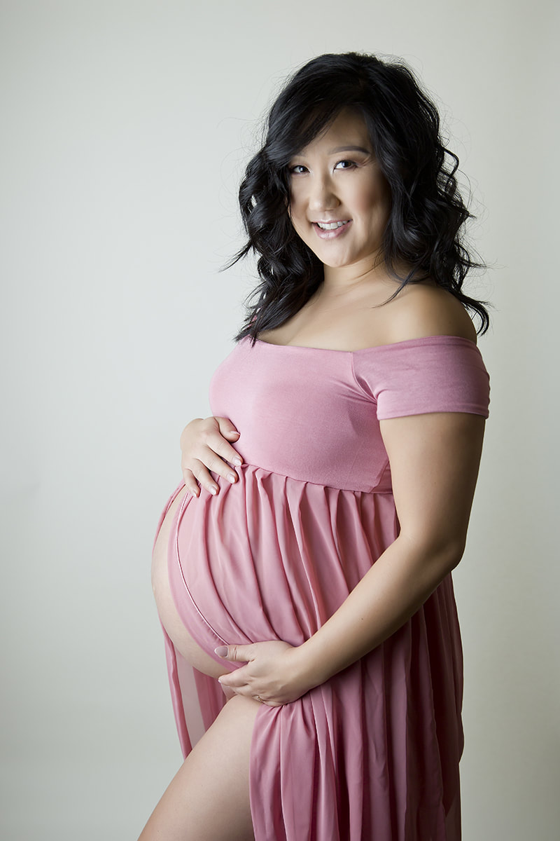 Woman in pink dress holding pregnant belly, white backdrop